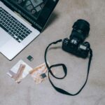 Overhead view of a camera and laptop with photos and memory cards on a marble surface.